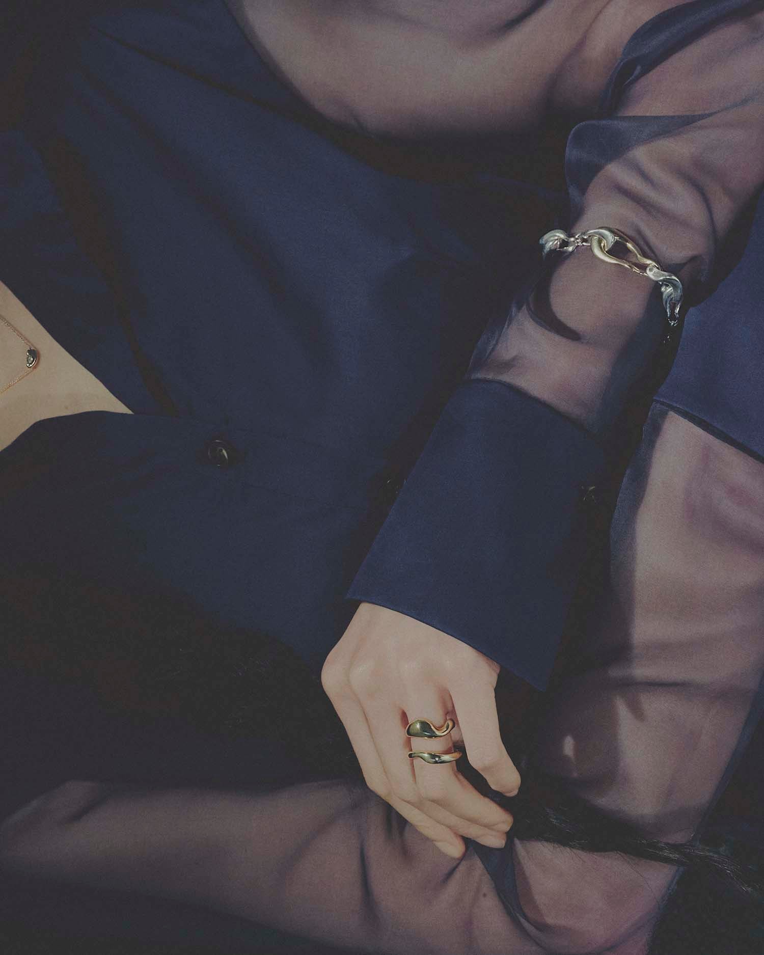 Close-up of a person wearing a gold bracelet and rings on a dark background