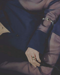 Close-up of a person wearing a gold bracelet and rings on a dark background