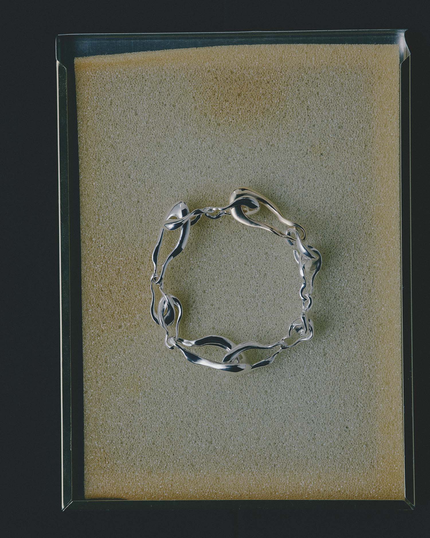 Silver bracelet on a textured beige sponge with a black border