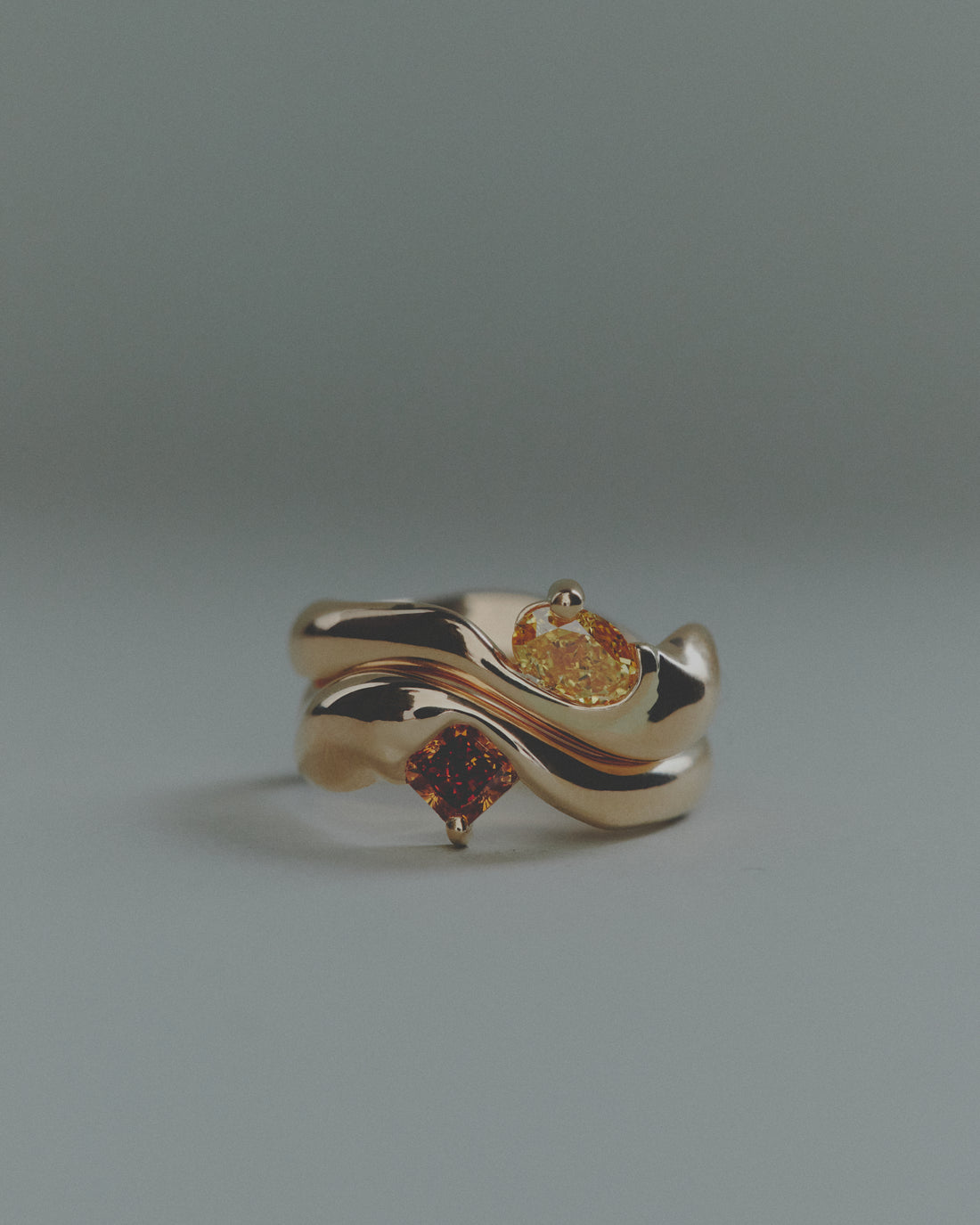 Two gold rings with embedded gemstones on a gray background