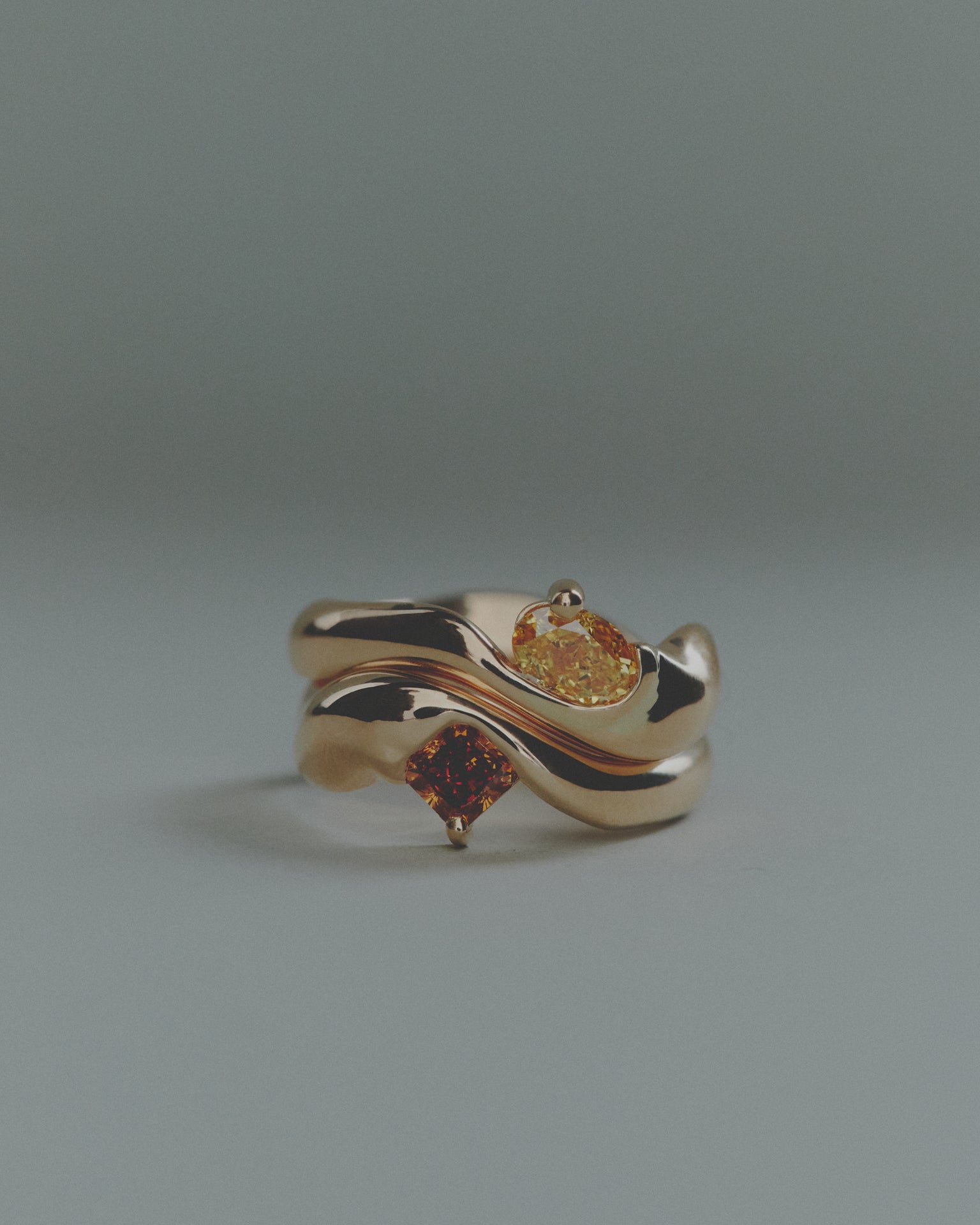 Two gold rings with embedded gemstones on a gray background