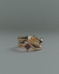 Two gold rings with embedded gemstones on a gray background