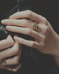 Close-up of hands with rings holding dark hair against a dark background