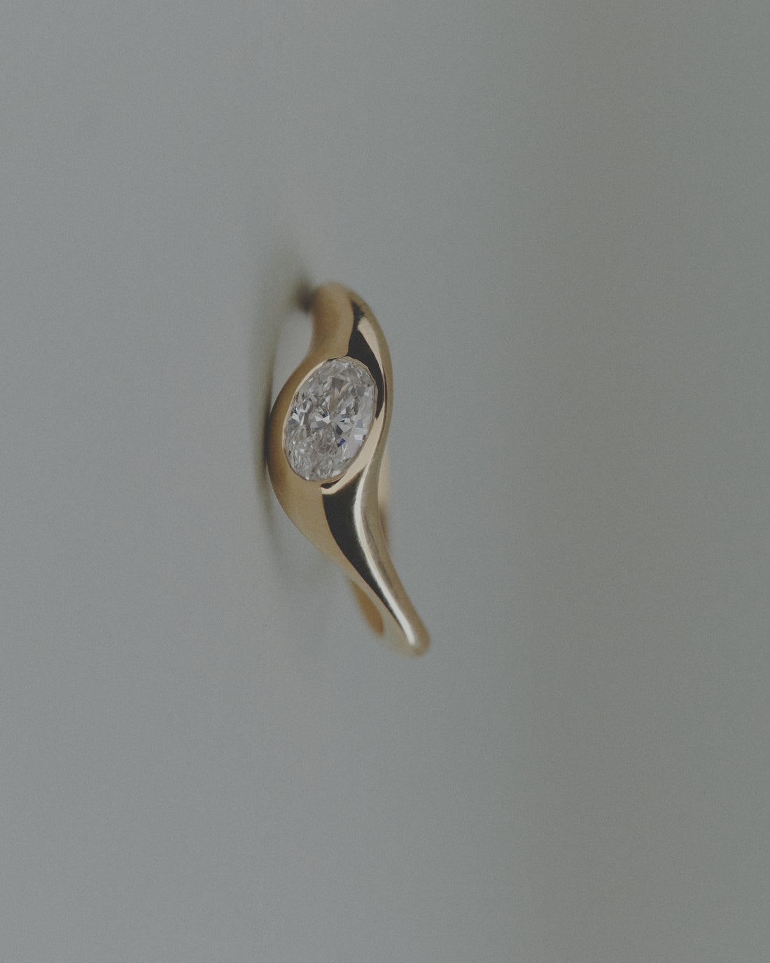 Gold ring with an oval diamond on a light gray background