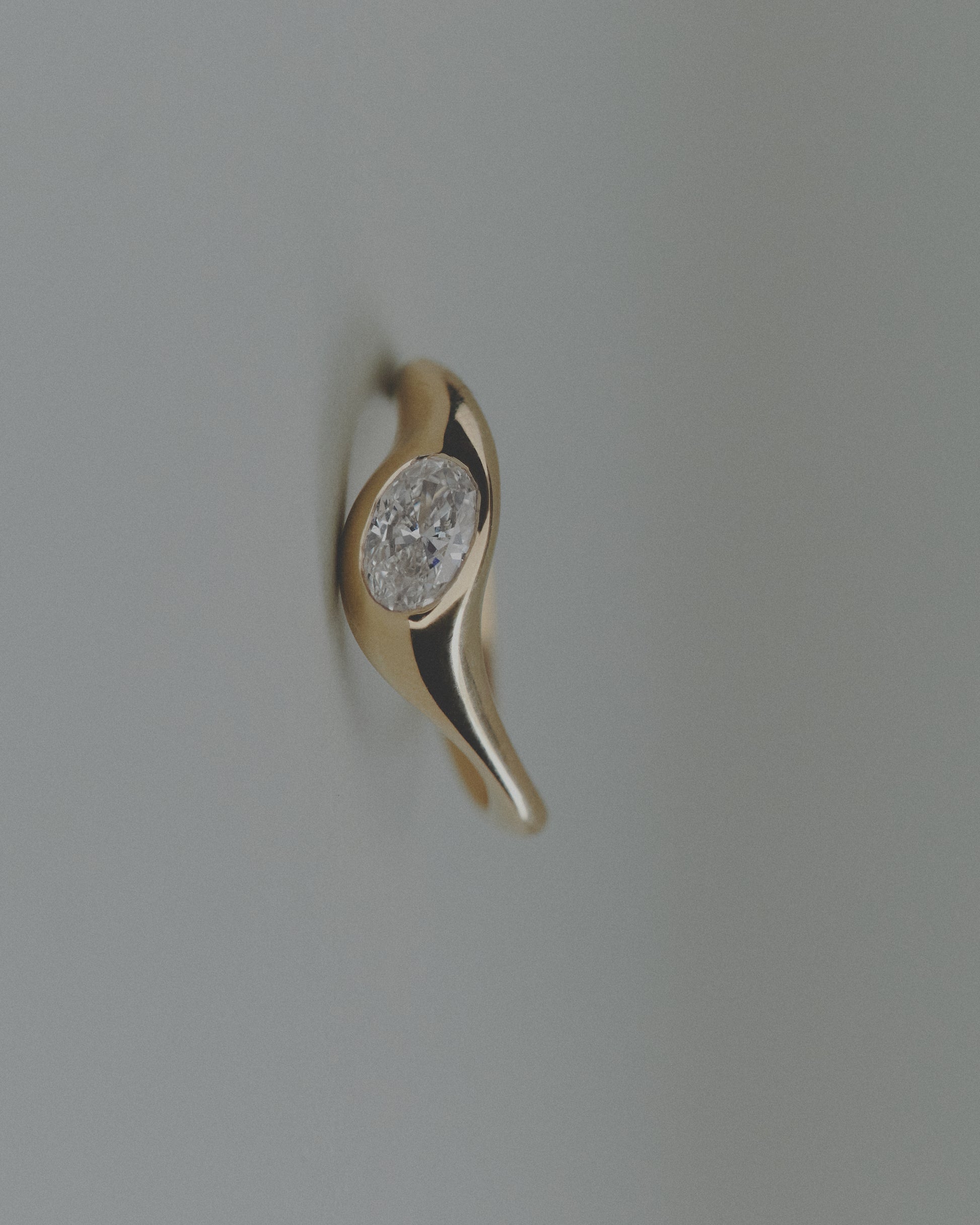 Gold ring with an oval diamond on a light gray background