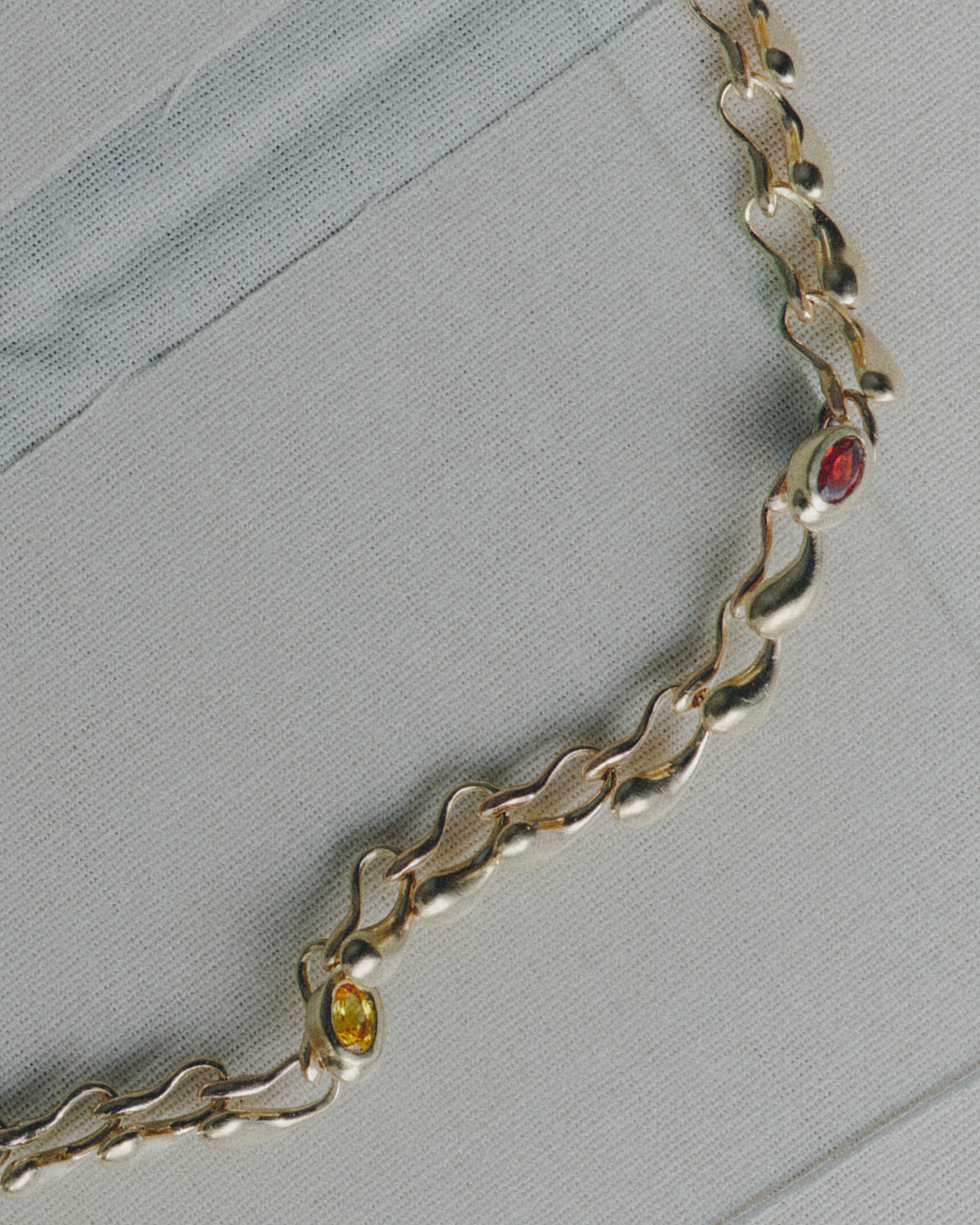 Gold necklace wiith embedded red and orange gemstones on a light gray background