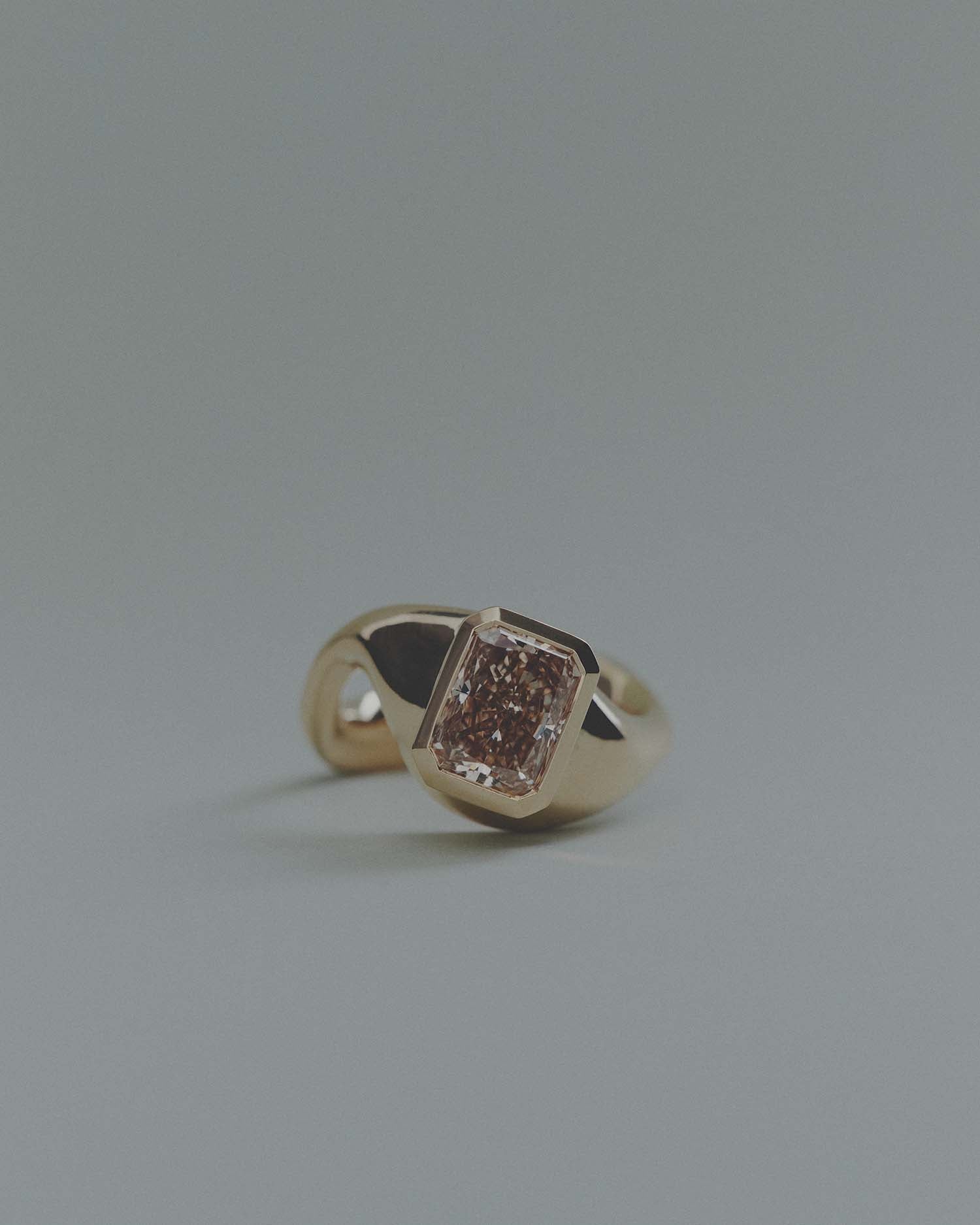 Gold ring with a unique design and large rectangular brown diamond on a gray background