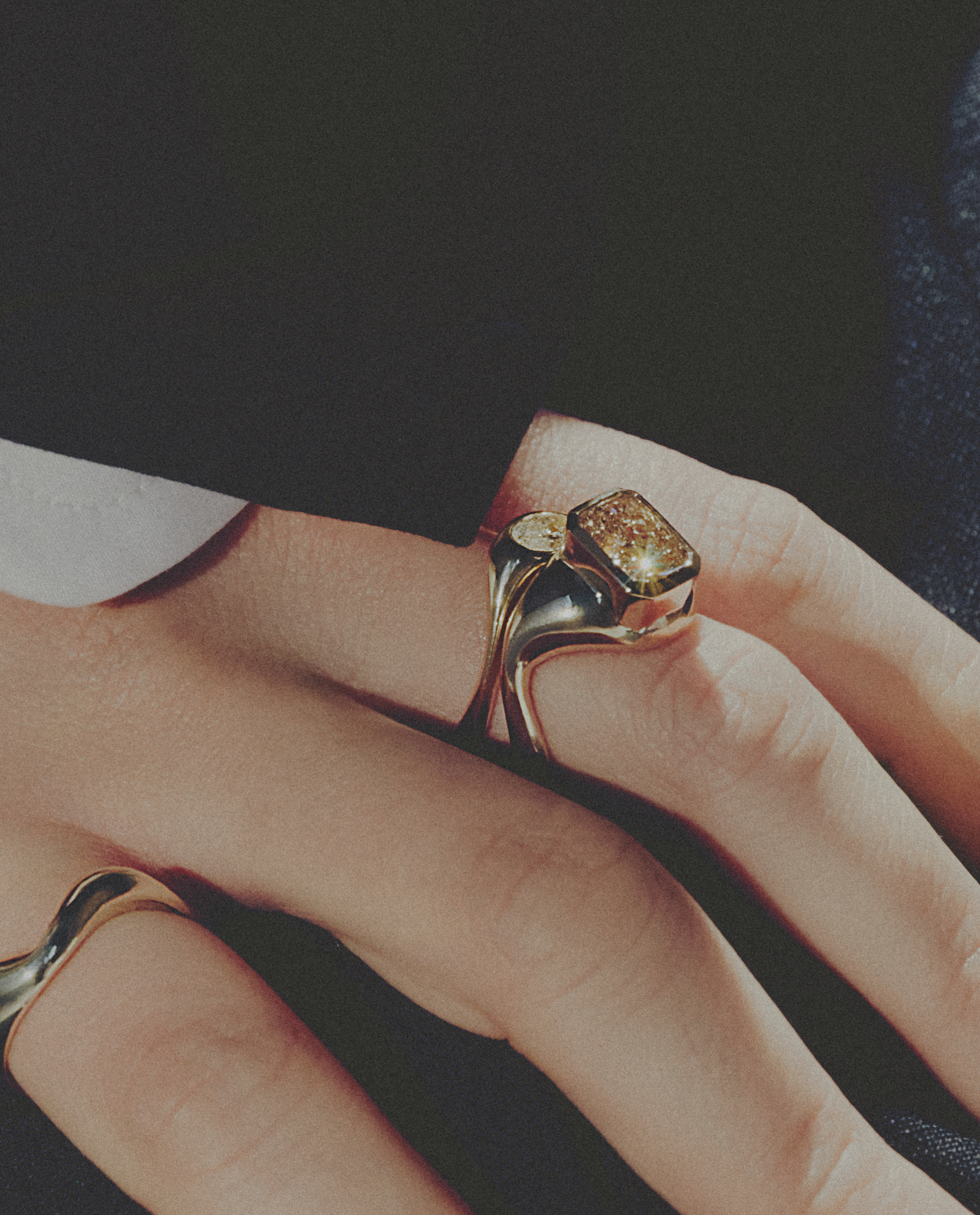 Close-up of a hand wearing a gold ring with a diamond on a dark background